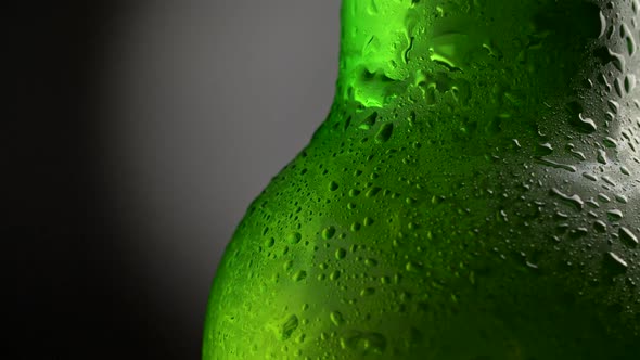 Green Beer Bottle Covered with Water Drops Rotating Against Dark Background. Close-up Shot, FHD