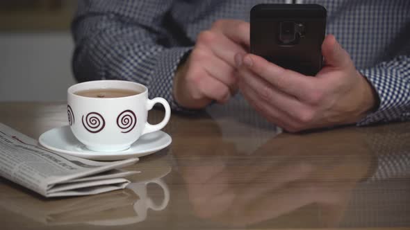 A man in a plaid shirt sits at a table and holds a phone in his hands