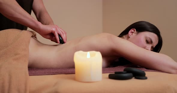 Young and Beautiful Woman Gets Hot Stone Massage Therapy in the Spa Salon