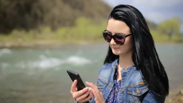 Young Brunette Girl in a Denim Jacket She Uses a Smartphone