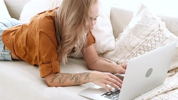 young girl lying on sofa at home and typing on a laptop.  and talks on video.