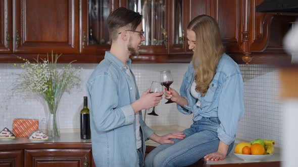 Carefree Beautiful Young Woman Sitting on Kitchen Countertop As Handsome Man Toasting