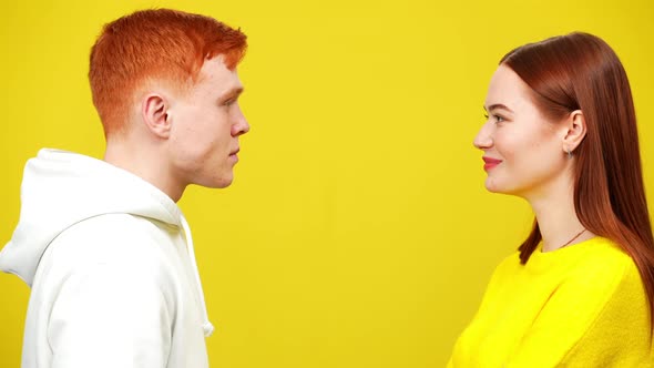 Young Millennial Redhead Couple Looking at Each Other at Yellow Background Smiling