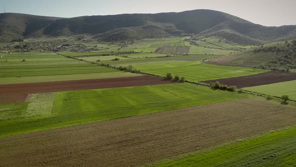 Aerial view of grass fields surrounded by vegetation and hills.