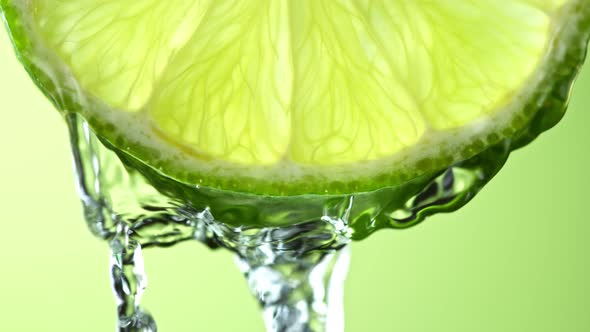 Super Slow Motion Macro Shot of Flowing Water From Lime Slice on Green Background at 1000Fps