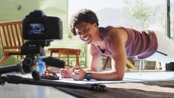 Happy fit african american man exercising at home, doing press ups and filming fitness vlog