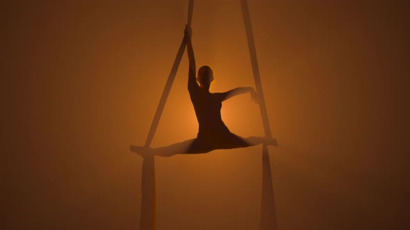 Silhouette of a Graceful Aerial Gymnast Performing Acrobatic Stunts and Twine on Aerial Silk