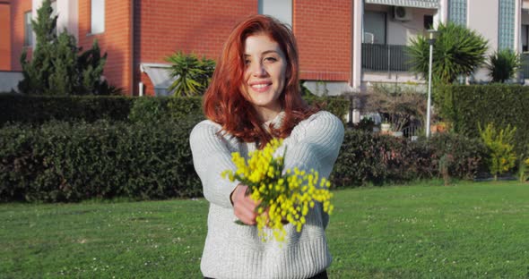 Young Girl Raises a Small Bouquet of Yellow Mimosas in a Park