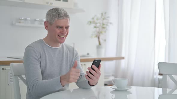 Senior Old Man Celebrating Success on Smartphone at Home