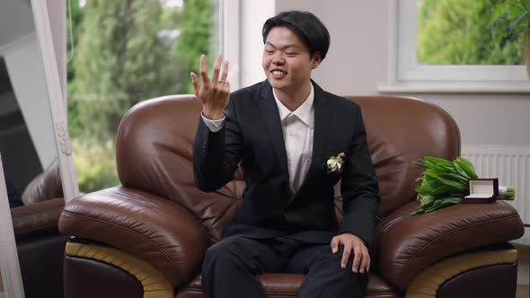 Joyful Newlywed Asian Man with Toothy Smile Looking at Camera Waving Showing Ring on Finger