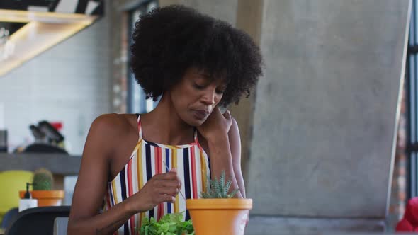 African american woman sitting in cafe eating salad and looking through window