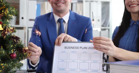 Man and Woman Waving Sparklers Near New Year Tree and Holding Documents Business Plan 2022  Movie