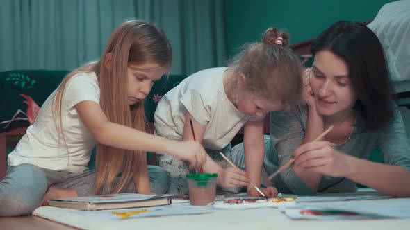 Happy young mother paint with her two daughters on the floor at home	 alt
