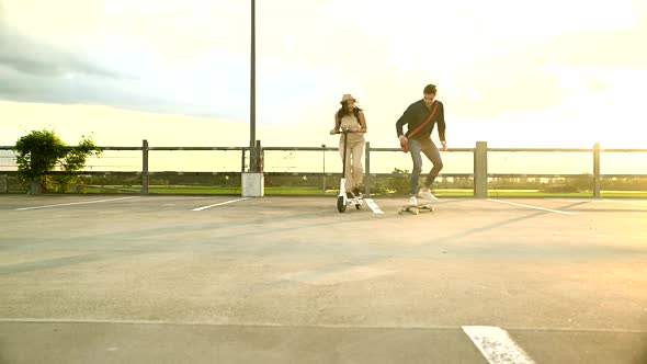 Young couple riding on longboard and electric scooter