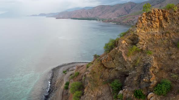 Aerial drone lowering over rocky outcrop with winding coastal tracks and crystal clear ocean water v