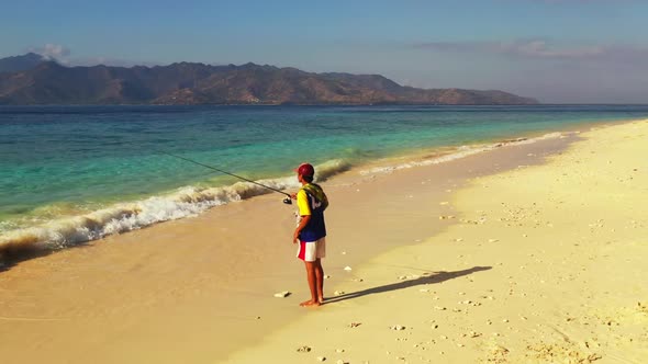 Man fishing on beautiful seashore beach wildlife by turquoise sea and white sand background of Gili 