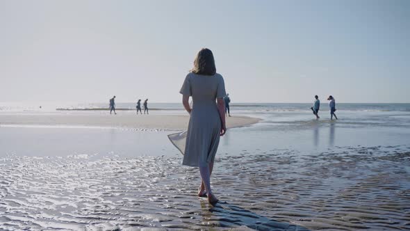 Woman Walks on Beach with Watery Pools Leading to the Ocean on a Windy Sunny Day