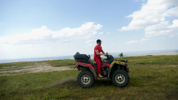 Man in a Black Cap and Red T-shirt on a Colored ATV Rides