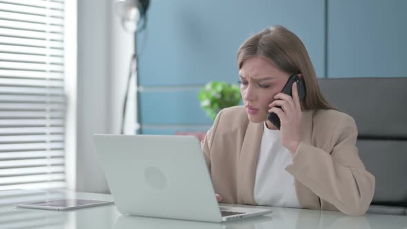 Angry Businesswoman Talking on Phone While Using Laptop in Office