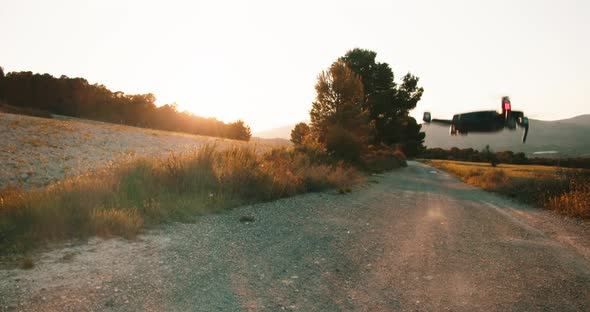 Tilt up shot of flying drone over golden fields and path in wilderness at sunset.