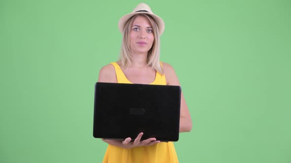 Happy Young Blonde Tourist Woman Talking While Using Laptop