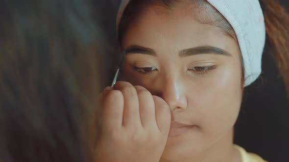 Close up of make up artist fixing the eyebrows on beautiful young woman