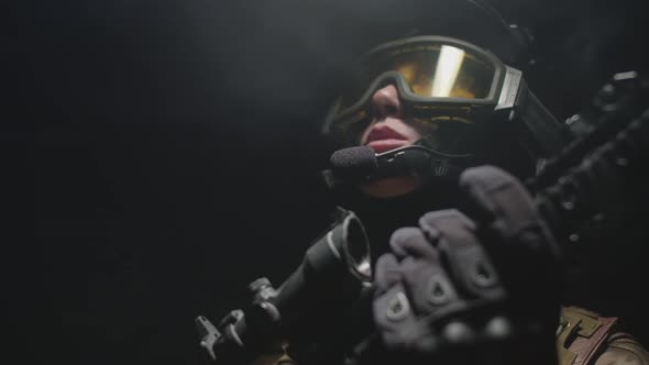 Soldier Woman in Modern Ammunition Dark and Foggy Room Looks Around at the Tops and Communicates alt