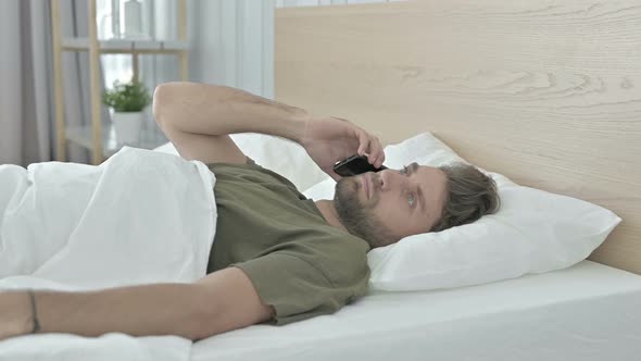 Shocked Young Man Talking on Cellphone in Bed