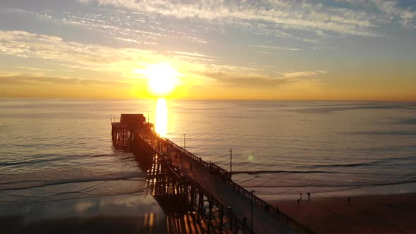 Drone shot over the Newport Beach pier in California at sunset on the pacific ocean water as people
