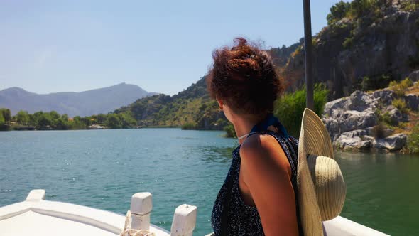 A Brunette in a Hat Sailing in a White Boat Along the Dalyan River and Enjoys the Mountain Landscape