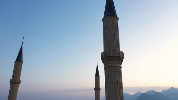 Three Mosque Minarets on Sunset Sky and Mountains Background