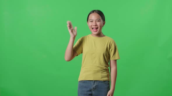 The Happy Young Asian Kid Girl Waving Hand And Say Bye Bye While Standing On Green Screen