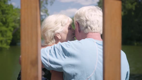 Back View of a Happy Mature Couple Sitting on the Bench Near the River, Admiring Nature