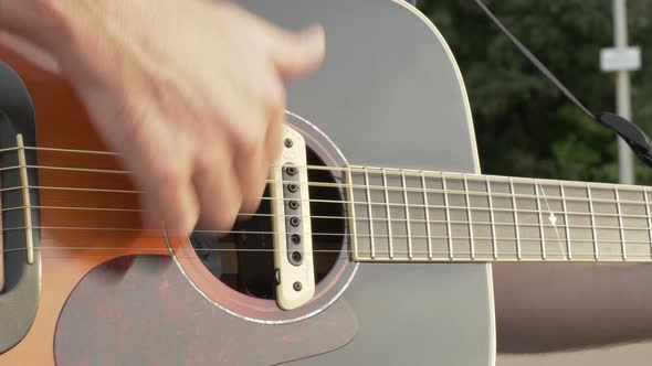 Close Up of a Man Energetically Strumming His Guitar Outside by a Road, Slow Pan