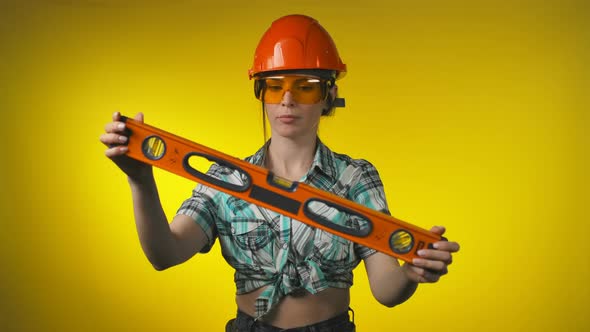 Girl Engineer Builder in an Orange Safety Helmet Holds a Building Level