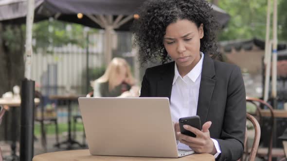 African Businesswoman Using Smartphone and Laptop in Outdoor Cafe