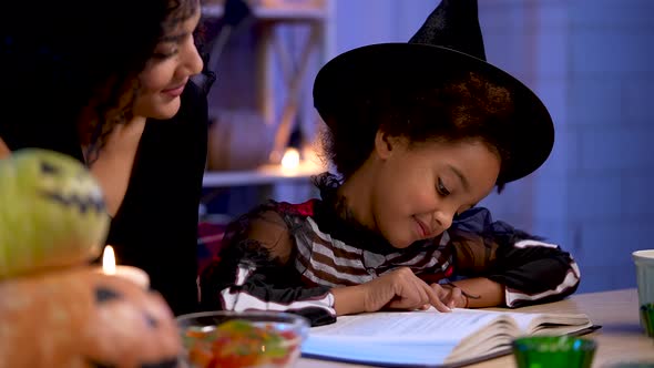 Little African American Girl in Festive Costume and Witch Hat Read Book