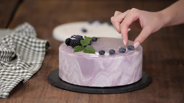 Women's hands decorate a berry mousse cake with with fresh berries on the kitchen table.
