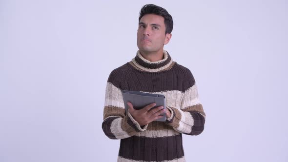 Young Happy Hispanic Man Thinking While Using Digital Tablet Ready for Winter