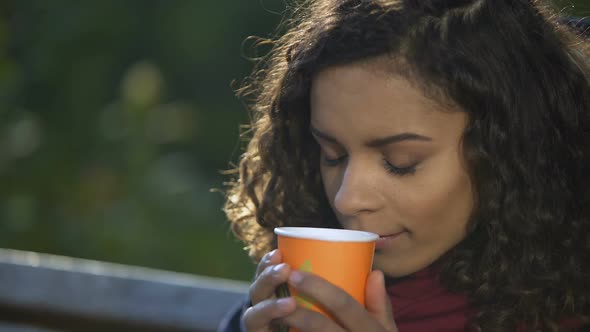 Young Curly-Haired Woman Enjoying Taste of Favorite Morning Coffee Outdoors