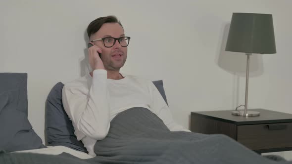 Angry Casual Man Talking on Smartphone While Sitting in Bed