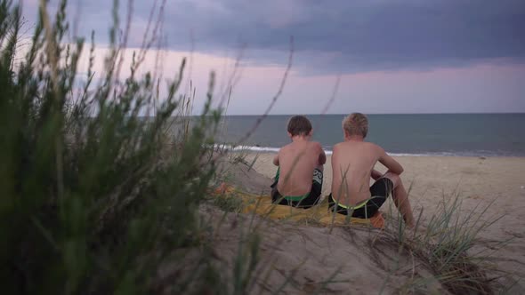 Portrait From Back of Two Friendly Caucasian Boys 1012 Hugging and Sitting at Seashore After