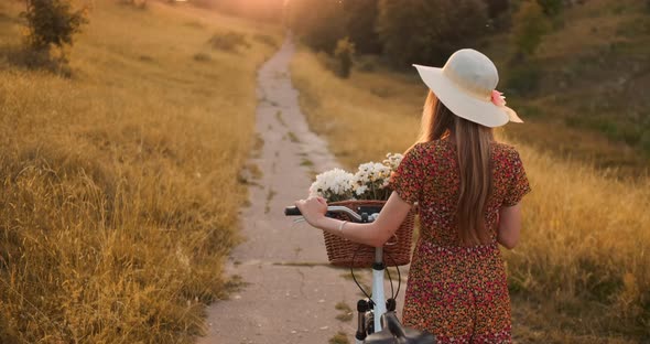 A Girl in a Hat with a Bicycle Turns Around and Looks at the Camera Smiling