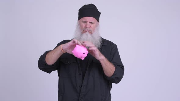 Mature Bearded Hipster Man Shaking Piggy Bank and Looking Sad