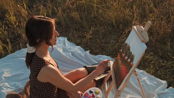 Young girl paints the picture on canvas in the countryside