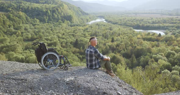 Handsome Smiling Lucky Young Disabled Man Sitting on the Stone on the Top of the Hill and Breathing