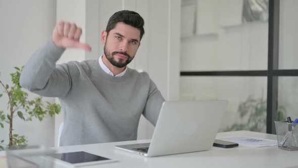 Young Man Showing Thumbs Down Sign While Using Laptop at Work