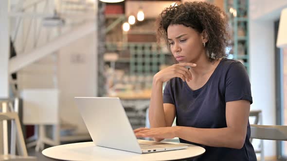 Pensive Young African Woman Using Laptop in Cafe