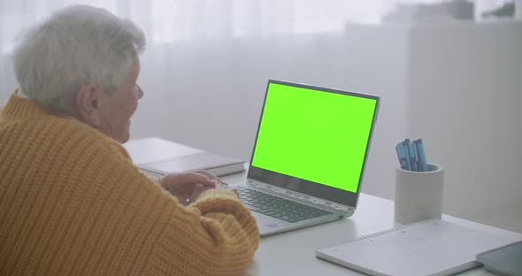 An Elderly Woman Looks at a Monitor with a Green Screen and Talks Via Video Link with Her