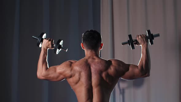 Athletic Shirtless Man Training His Hands Muscles with the Dumbbells  View From the Back